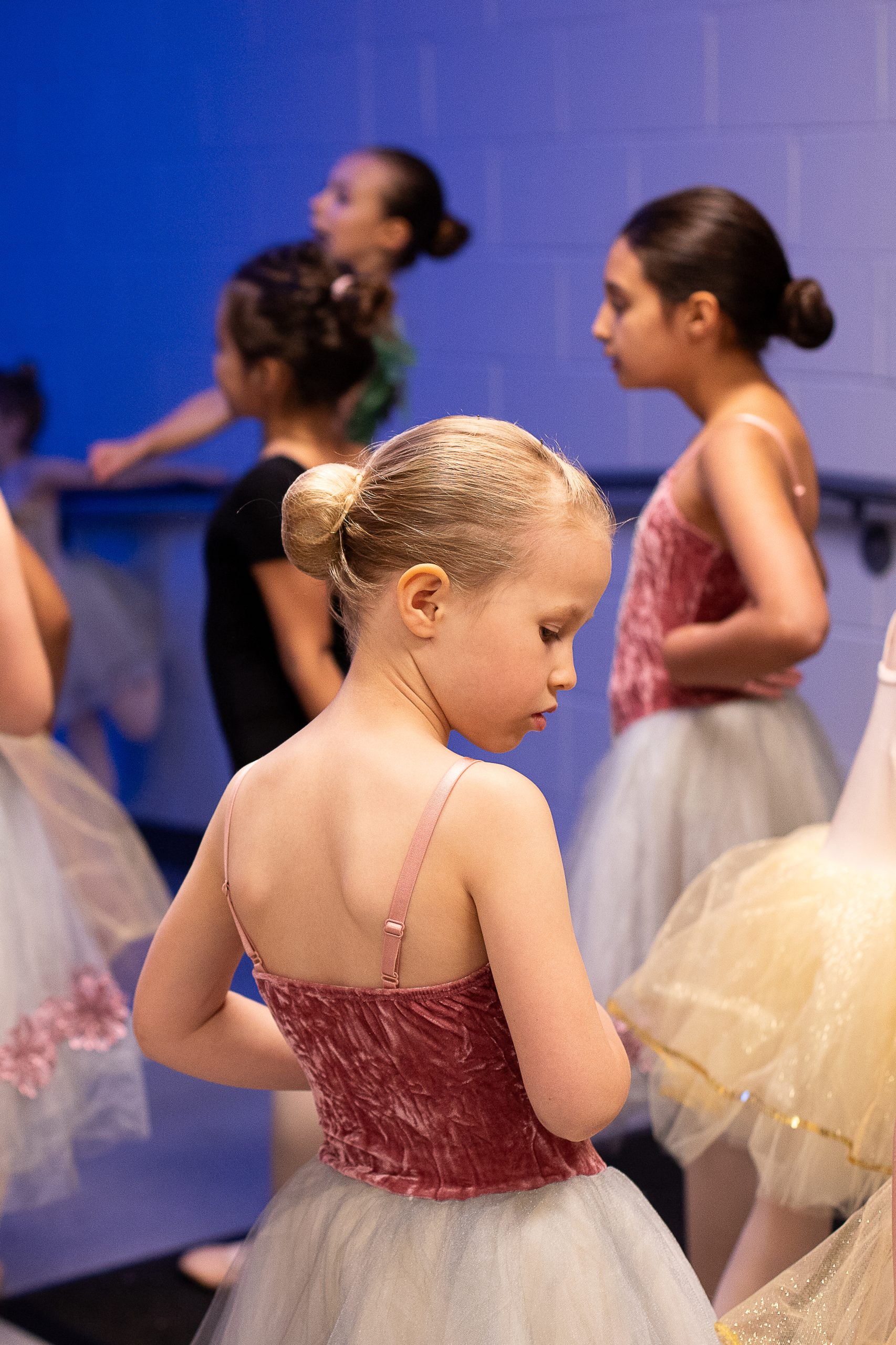 Young ballerina in pink and blue costume waits to backstage with other dancers before performing.