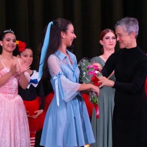 ballerina in blue Alice in Wonderland costume receives roses after performance. Director smiles and hands roses to ballerina