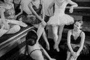 ballerinas in tutus sit and smile at one another in the dance studio