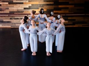 ballet dancers in pale blue costumes pose in a circle