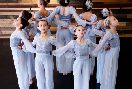 ballet dancers in pale blue costumes pose in a circle